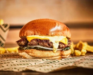 Close-up food photography of a cheeseburger with melted cheese, beef patty, pickles, and sauce in a brioche bun.