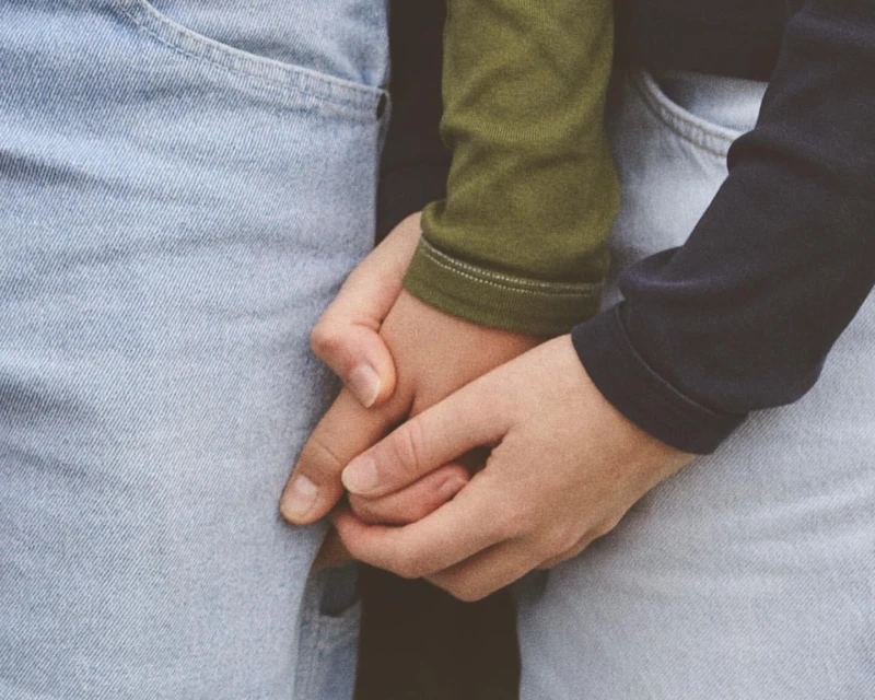 Close-up shot of two people holding hands, wearing long-sleeved shirts and jeans, creating a warm and intimate connection.
