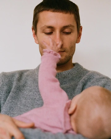A man holding a baby in a close-up shot, showcasing a soft, intimate moment with muted color tones, family portrait, and a plain background.