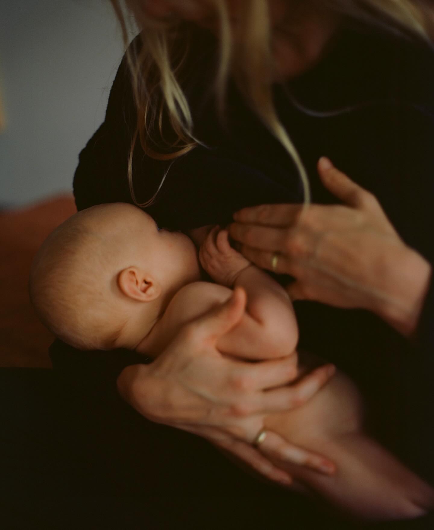 Close-up of a mother cradling and breastfeeding her baby indoors, showcasing a tender moment of maternal care in a softly lit scene.