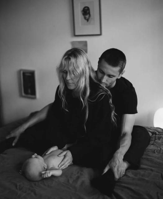 Monochrome portrait of a couple and baby on a bed with neutral tones and soft lighting, creating a peaceful and intimate scene.