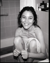 Black and white portrait of a smiling woman wrapped in a towel inside a tiled bathroom by Sophie Van Der Perre