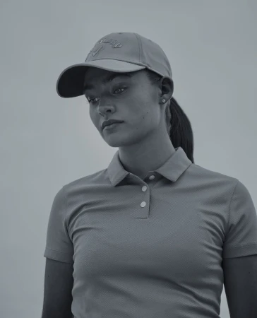 Close-up portrait of a woman wearing a collared polo shirt and a baseball cap against a clear sky background.