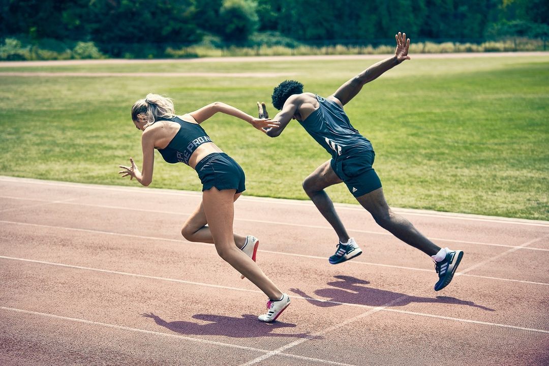 Two athletes, a man and a woman, are sprinting on a track on a sunny day, viewed from a medium distance. They are focused and determined.