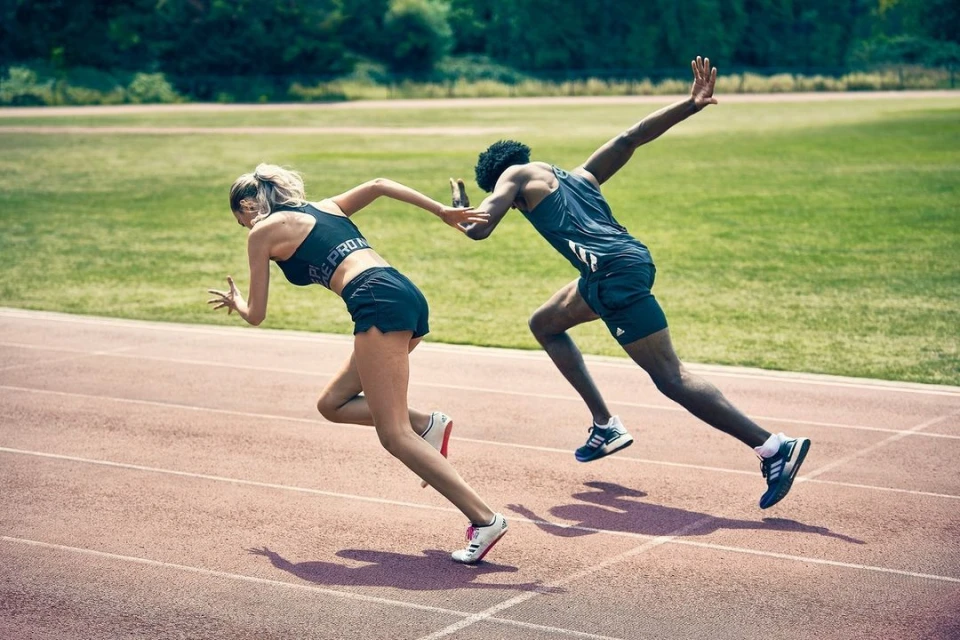 Two athletes, a man and a woman, are sprinting on a track on a sunny day, viewed from a medium distance. They are focused and determined.
