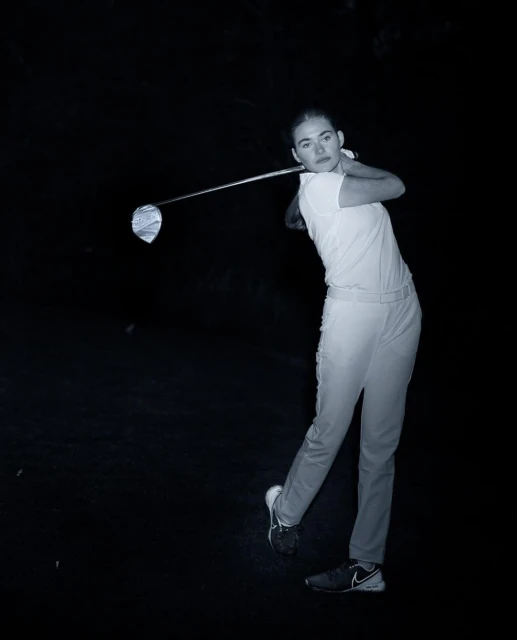 Monochrome shot of a woman swinging a golf club in a dark setting, focusing on her athletic form and the equipment.