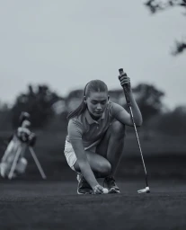 Female golfer crouching on a green putting a golf ball with a putter in hand, shot by Simon Stock.