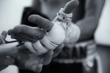 Close-up of hands wrapping athletic tape around a fighter's knuckles in black and white photography by Simon Stock.