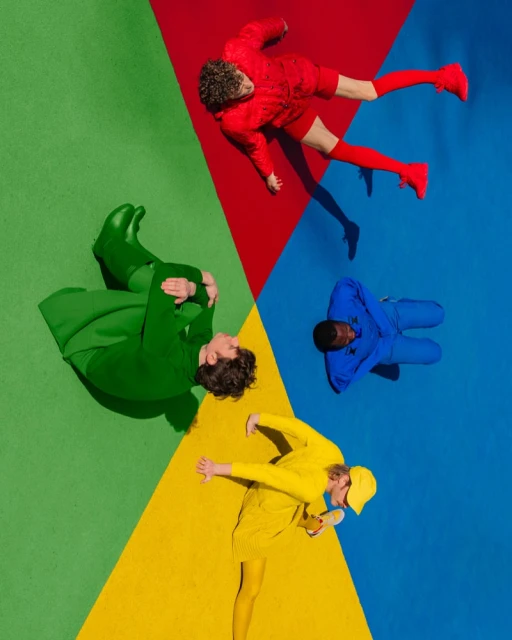 Overhead shot of four people lying on a color wheel background, each person dressed in a different primary color.