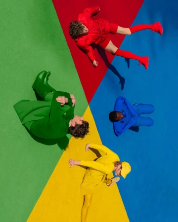 Overhead shot of four people lying on a color wheel background, each person dressed in a different primary color.