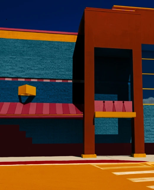 Abstract view of a colorful building with blue brick walls, orange accents, and a pink awning under a clear dark blue sky.