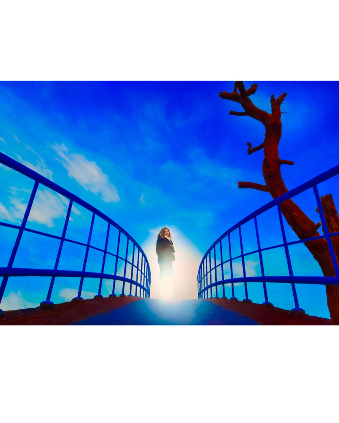 Woman standing on a blue bridge against a vibrant blue sky with light clouds, with a red-brown tree on the side, creating a surreal scene.