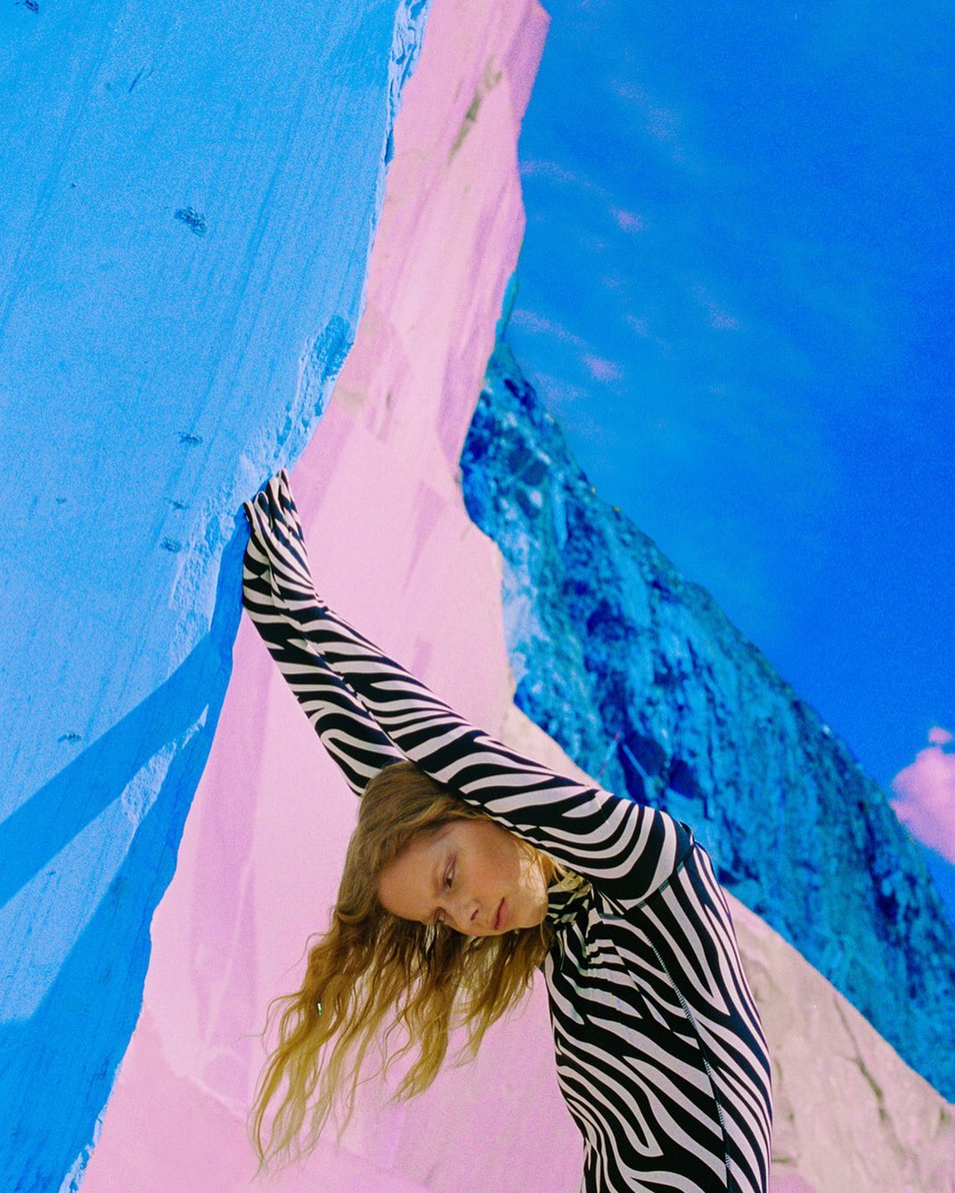 Woman in zebra-print bodysuit strikes a pose amid rock formations and a blue sky, creating a vibrant and surreal outdoor scene.