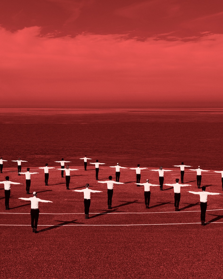 A large group of people with outstretched arms stand in a circle on a field, all colored in shades of red.