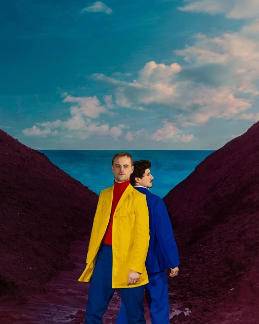 Two men in vibrant suits stand back-to-back against a landscape featuring a blue sea, sky, and converging burgundy-hued land formations.