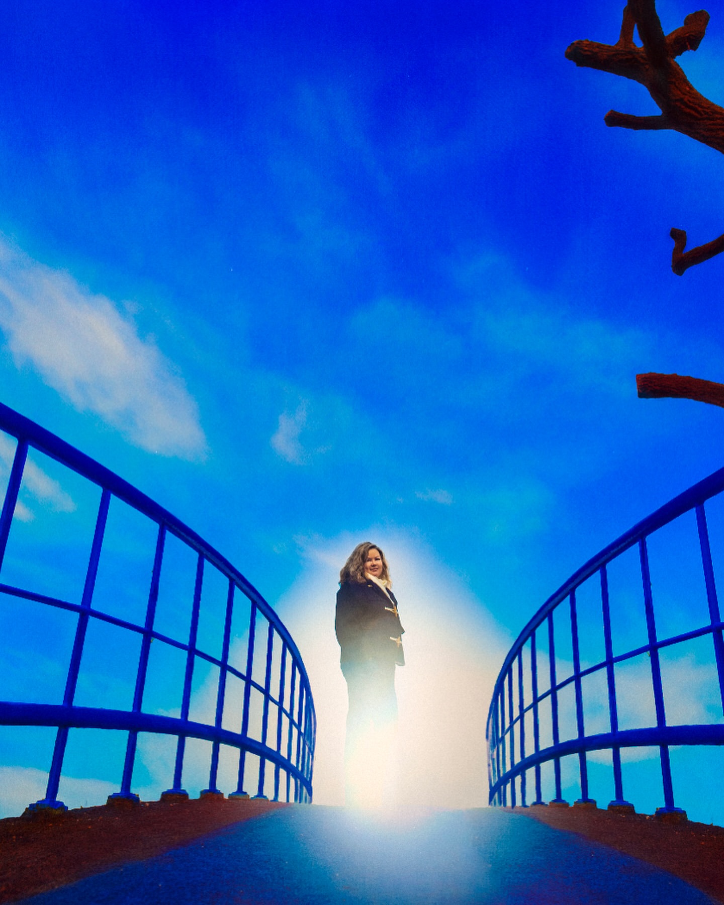 A woman stands on a blue bridge against a bright blue sky. The bridge is curved and made of metal, and the background is a dreamy scene.