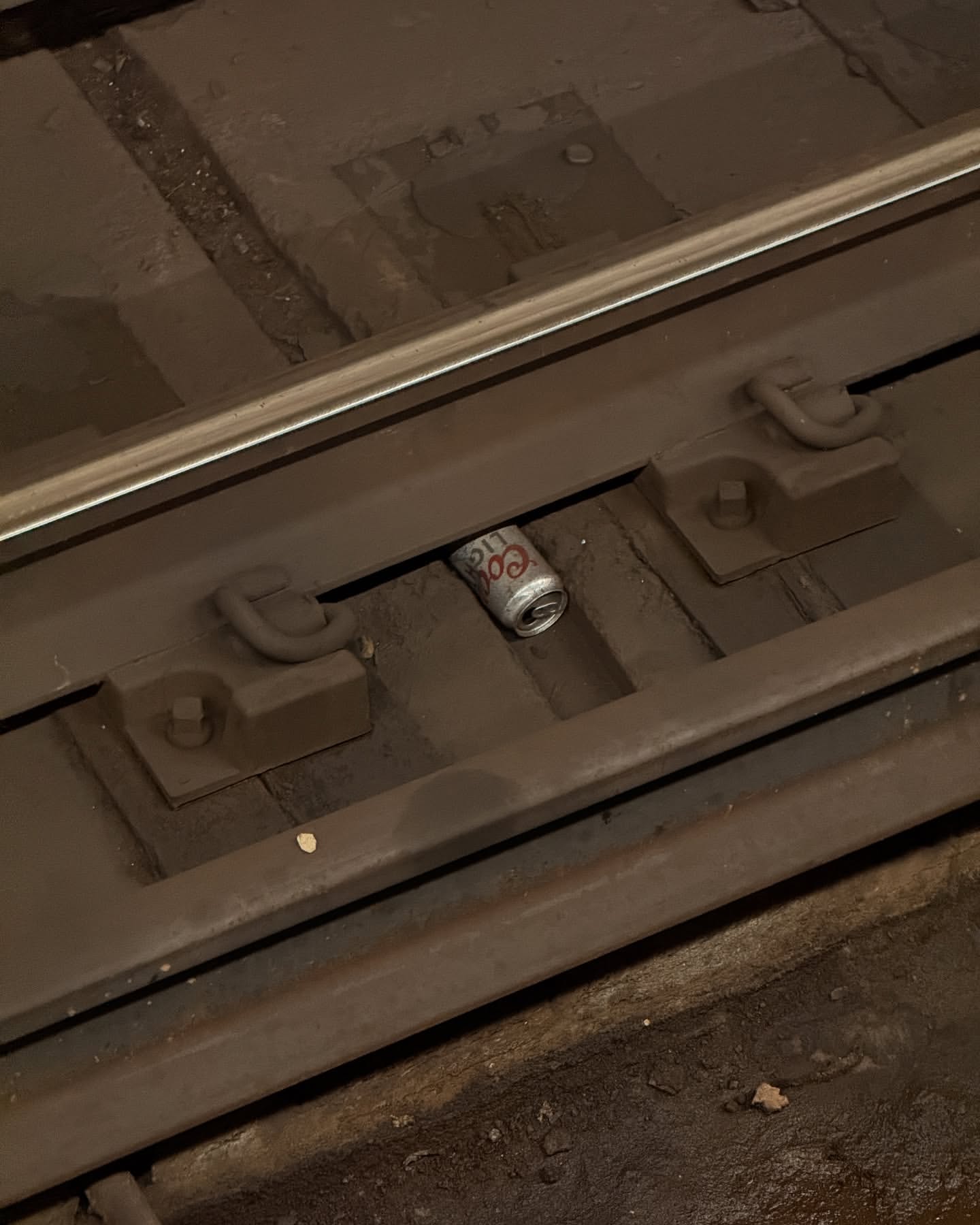 Discarded Coors Light beer can sits between the rails on a section of subway tracks, photographed in a medium, eye-level shot.