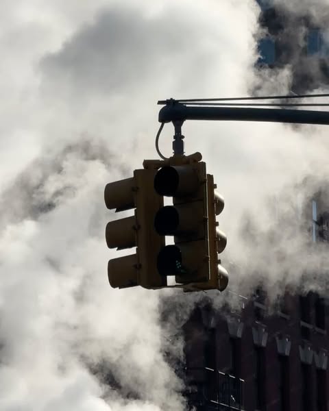 Downtown city view of a yellow traffic light hanging over street with urban steam rising on an overcast day in a business district.