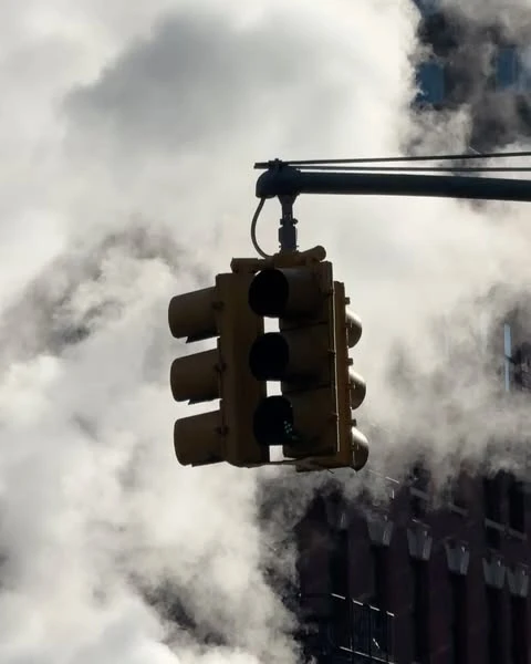 Downtown city view of a yellow traffic light hanging over street with urban steam rising on an overcast day in a business district.