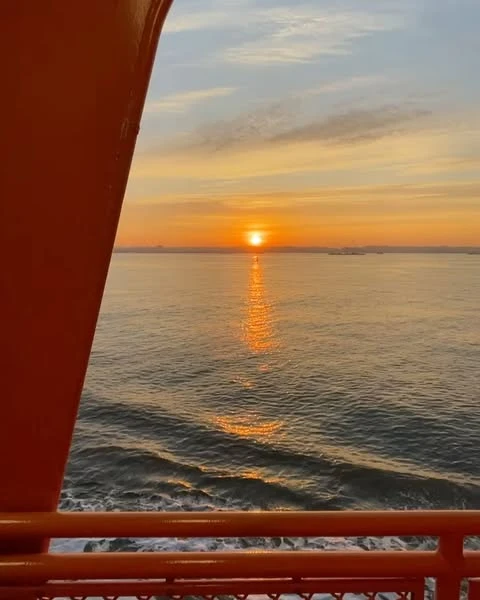 Sunset over the ocean with orange bridge in the foreground. The sky is filled with soft colors and the water reflects the sunlight.