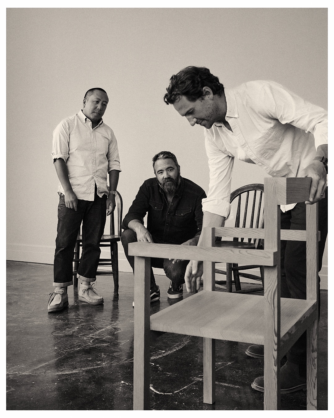 Three men in a bright studio setting, focusing on light-wood chairs with a minimalist design, showcasing furniture craftsmanship and design.