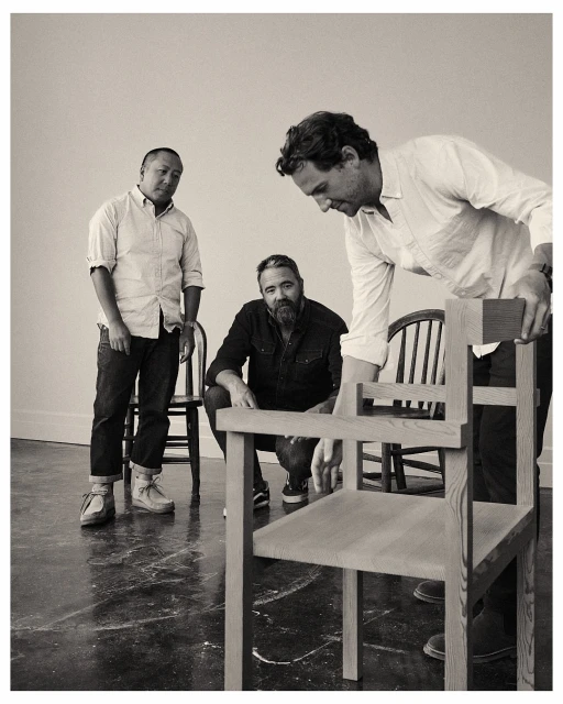 Three men in a bright studio setting, focusing on light-wood chairs with a minimalist design, showcasing furniture craftsmanship and design.