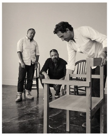 Three men in a bright studio setting, focusing on light-wood chairs with a minimalist design, showcasing furniture craftsmanship and design.