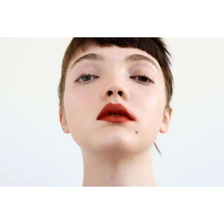 Close-up portrait of a woman with short dark hair, fringe, and bold red lipstick against a plain white background.