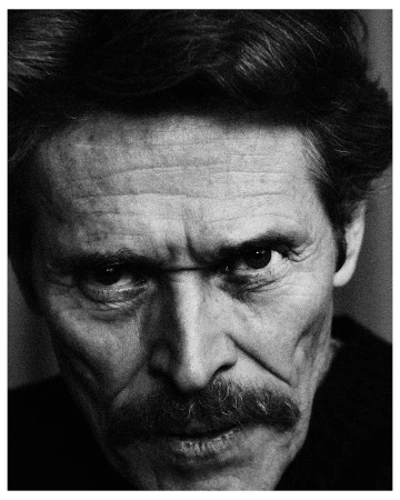 Close-up black and white portrait of actor Willem Dafoe with dark hair and a mustache looking directly at the camera