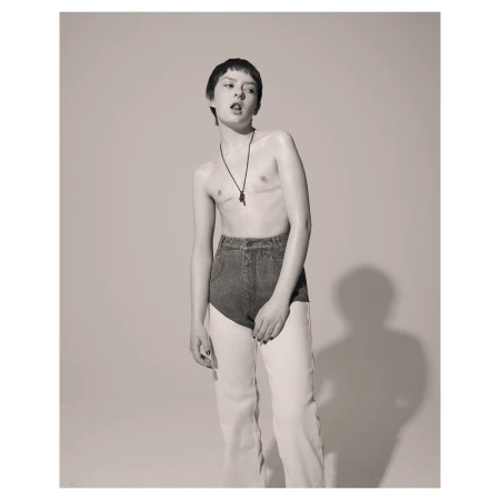 Portrait of a person with short dark hair wearing high-waisted denim pants against a plain studio background.