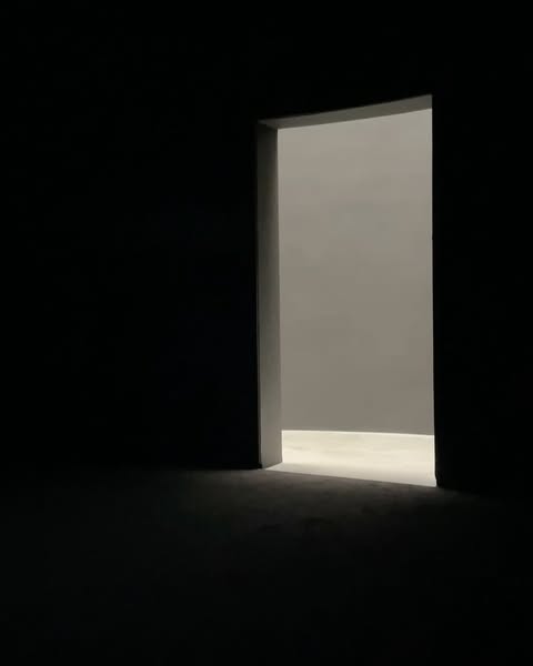 Illuminated doorway with light casting into dark room. The light leads to a bright room beyond the opening, contrasting with shadows.