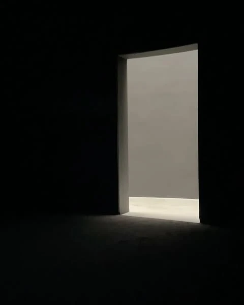 Illuminated doorway with light casting into dark room. The light leads to a bright room beyond the opening, contrasting with shadows.