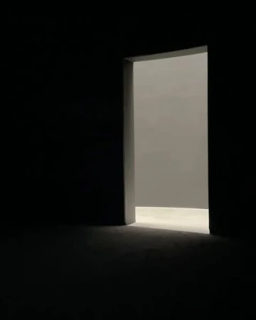 Illuminated doorway with light casting into dark room. The light leads to a bright room beyond the opening, contrasting with shadows.