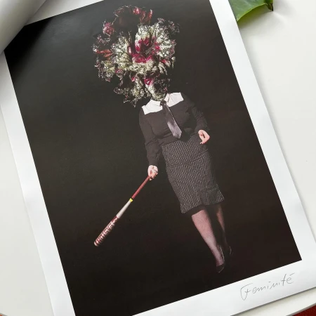 Surreal portrait of person with flower head in dark clothing holding a baseball bat in a studio setting against a black background.