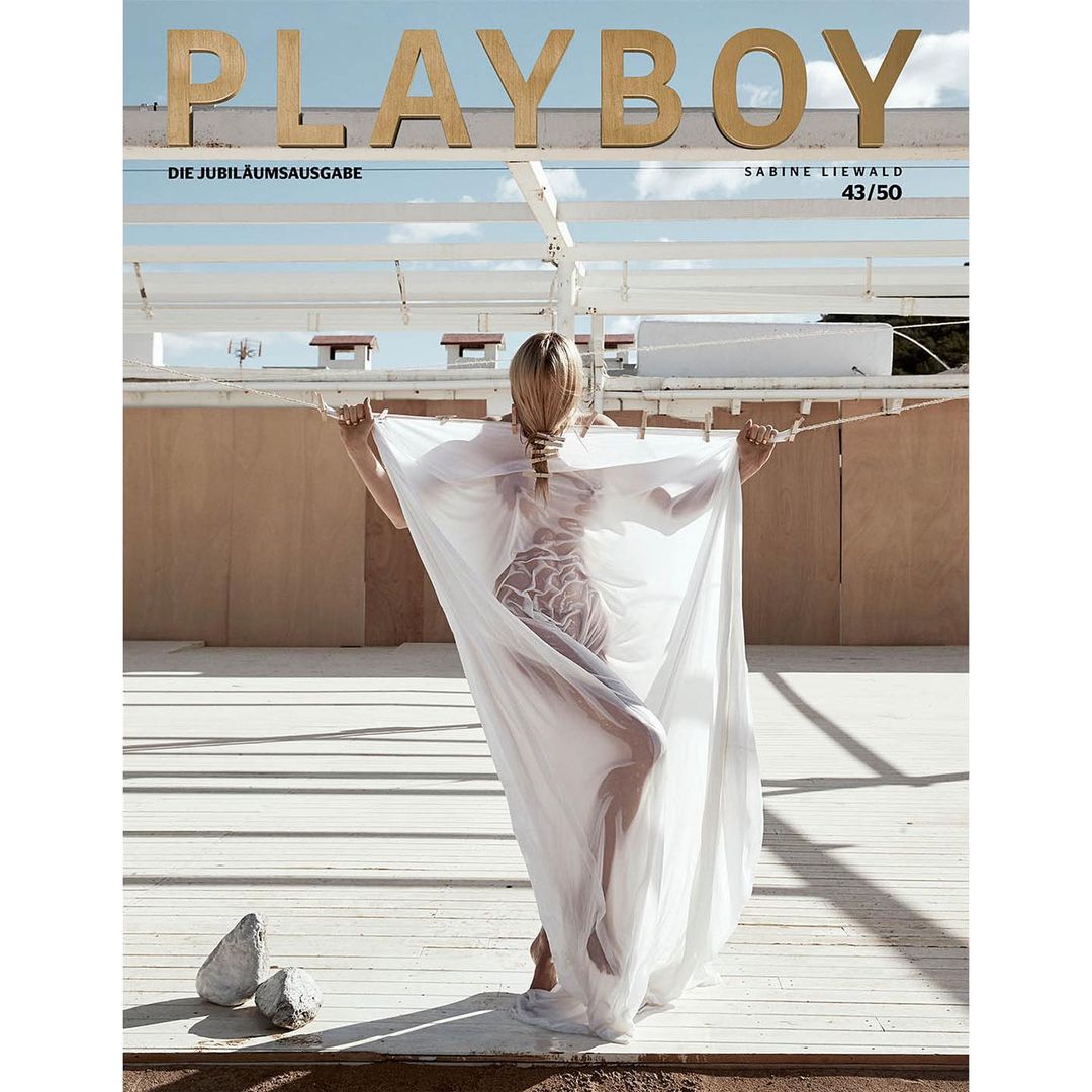 Playboy magazine cover featuring a blonde woman in a sheer white garment on an outdoor terrace against a light brown wall and blue sky.