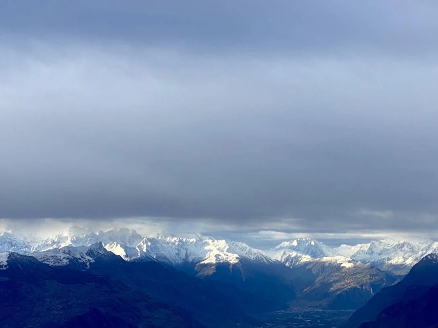 Snow-covered mountains stretch across the horizon beneath a sky filled with soft, diffused light, creating a serene landscape.