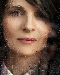 Close-up portrait of a woman viewed through a glass surface covered in glistening water droplets