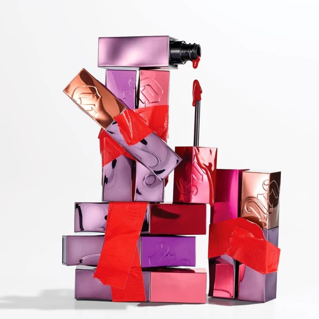 Stacked lipstick tubes in various colors with red tape accents against a clean white background, beauty product concept.