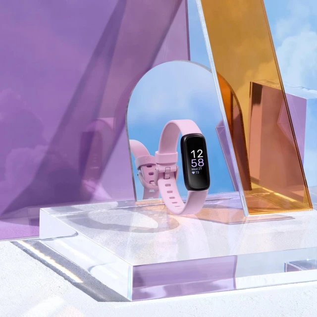 Close-up studio shot of a pink fitness tracker on a clear acrylic platform, reflecting against colorful geometric mirrors.