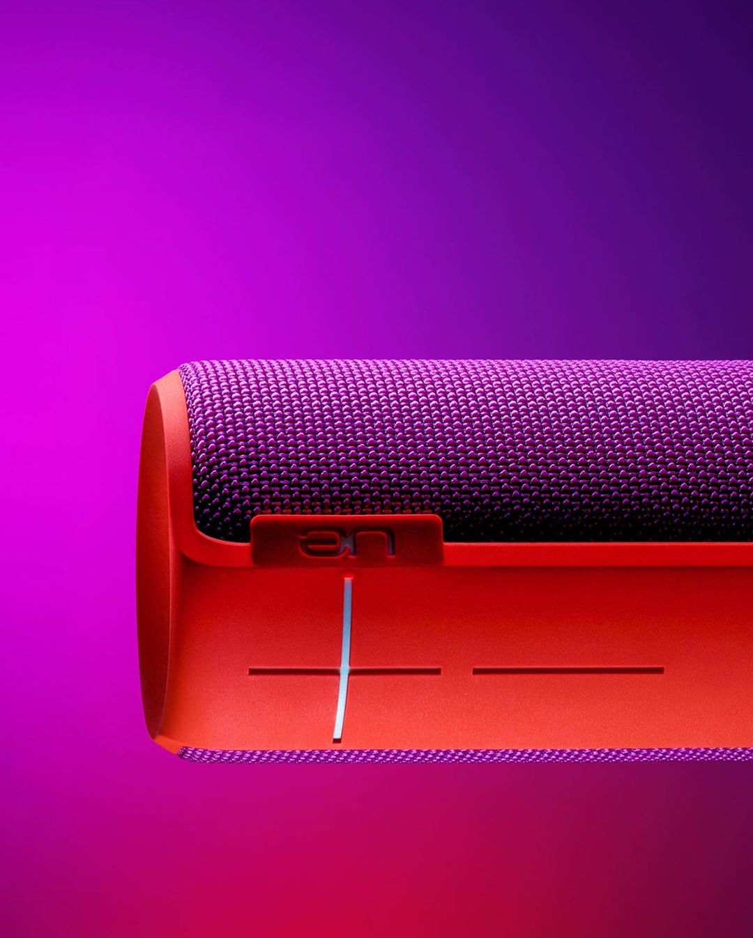 Close-up of a purple and orange portable speaker on a purple background, highlighting the speaker's design and texture.