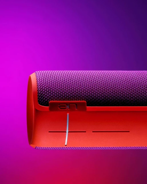 Close-up of a purple and orange portable speaker on a purple background, highlighting the speaker's design and texture.