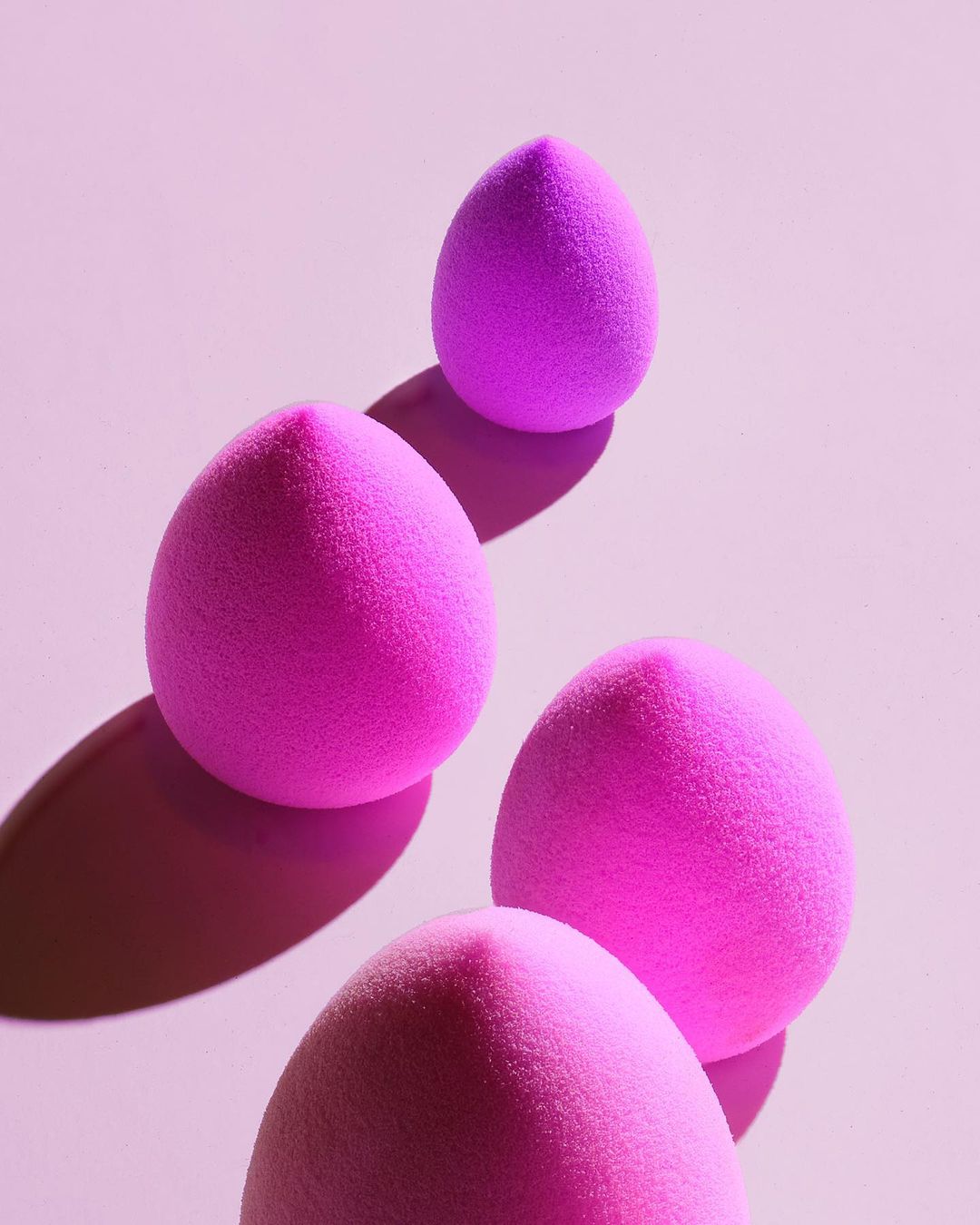 Close-up shot of a collection of four pink makeup sponges on a pink background, creating a visually appealing beauty product display.