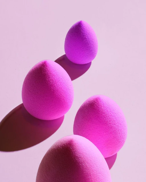 Close-up shot of a collection of four pink makeup sponges on a pink background, creating a visually appealing beauty product display.