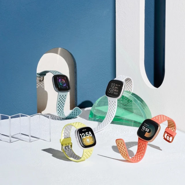 Studio shot of a group of colorful smart watches with perforated bands against a split light blue and white backdrop, showcasing wearable tech.