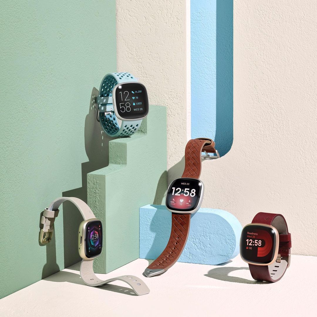 Four smartwatches with varied bands on stepped display. Fitness trackers show digital time against color block and gradient background.