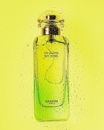Perfume bottle of Hermes' Un Jardin Sur Le Nil on yellow background with water droplets conveys fresh, light, and premium product.