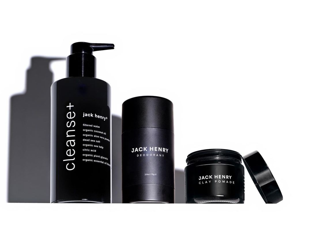 A trio of Jack Henry men's grooming products in black bottles against a bright white background, including cleanser, deodorant, and clay pomade.