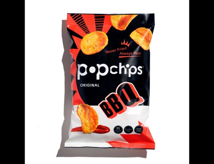 Close-up of a bag of Popchips BBQ flavour snack on a white surface, showcasing the product and its branding against a studio backdrop.
