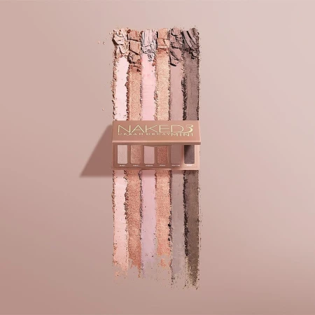 Naked 3 Urban Decay Mini eyeshadow palette displayed with color swatches in shades of nude, pink, beige and brown on neutral background.