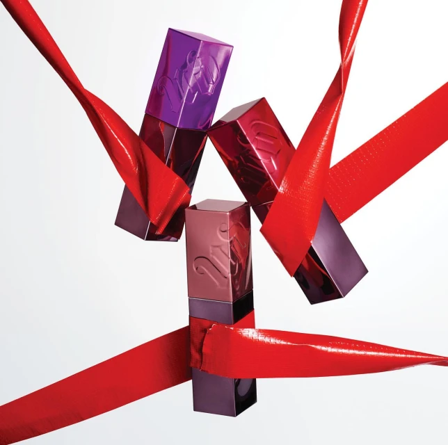 Three colorful lipstick tubes with a red ribbon against a white background, product photography for beauty or cosmetics marketing.